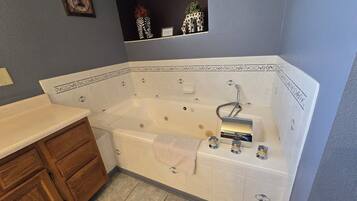 A bathroom with a freestanding bathtub, wooden cabinets, and a small shelf with decorative items.