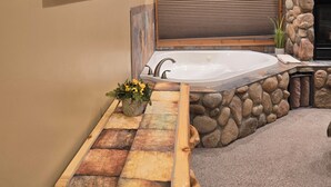 A bathroom with a stone wall, a wooden bench, a bathtub, and a mounted television. - Buffalo Peaks B&B (Buena Vista)