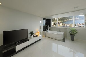 Un baño moderno con una bañera grande, un televisor y vistas al mar.