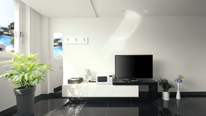 A modern living room with a flat-screen TV, a potted plant, a microwave, and a small table with a lamp. - Doya Family Hotel (Geoje)
