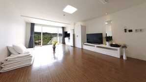 A modern living room with a flat-screen TV, a white entertainment unit, and a large window with a view of the outdoors. - Doya Family Hotel (Geoje)