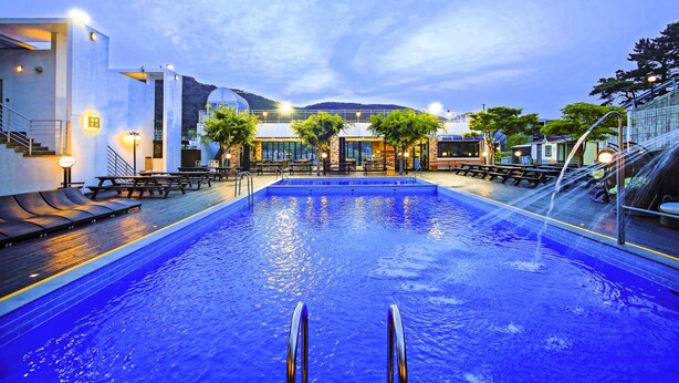 A swimming pool with a view of a modern building and a mountain in the background. - Doya Family Hotel (Geoje)