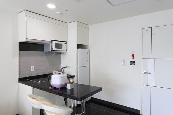 A compact kitchen with white cabinets, a black countertop, a microwave, a refrigerator, and a sink.