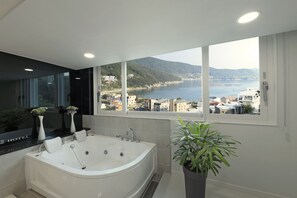Un baño moderno con una bañera grande, un espejo y vistas a un pueblo costero.
