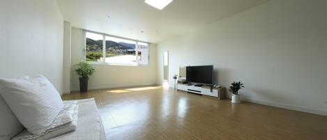A modern living room with a large window, a flat-screen TV, and a wooden floor.