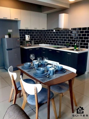 A modern kitchen with dark blue cabinets, a white countertop, and a dining area set with blue plates and glasses.