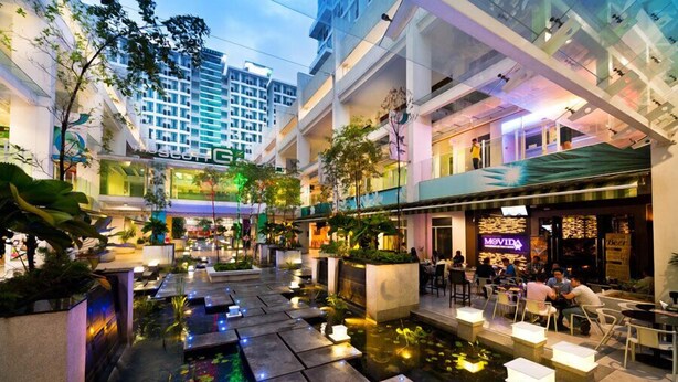Un moderno atrio interior con una fuente central, zonas de estar y varias tiendas y restaurantes.
