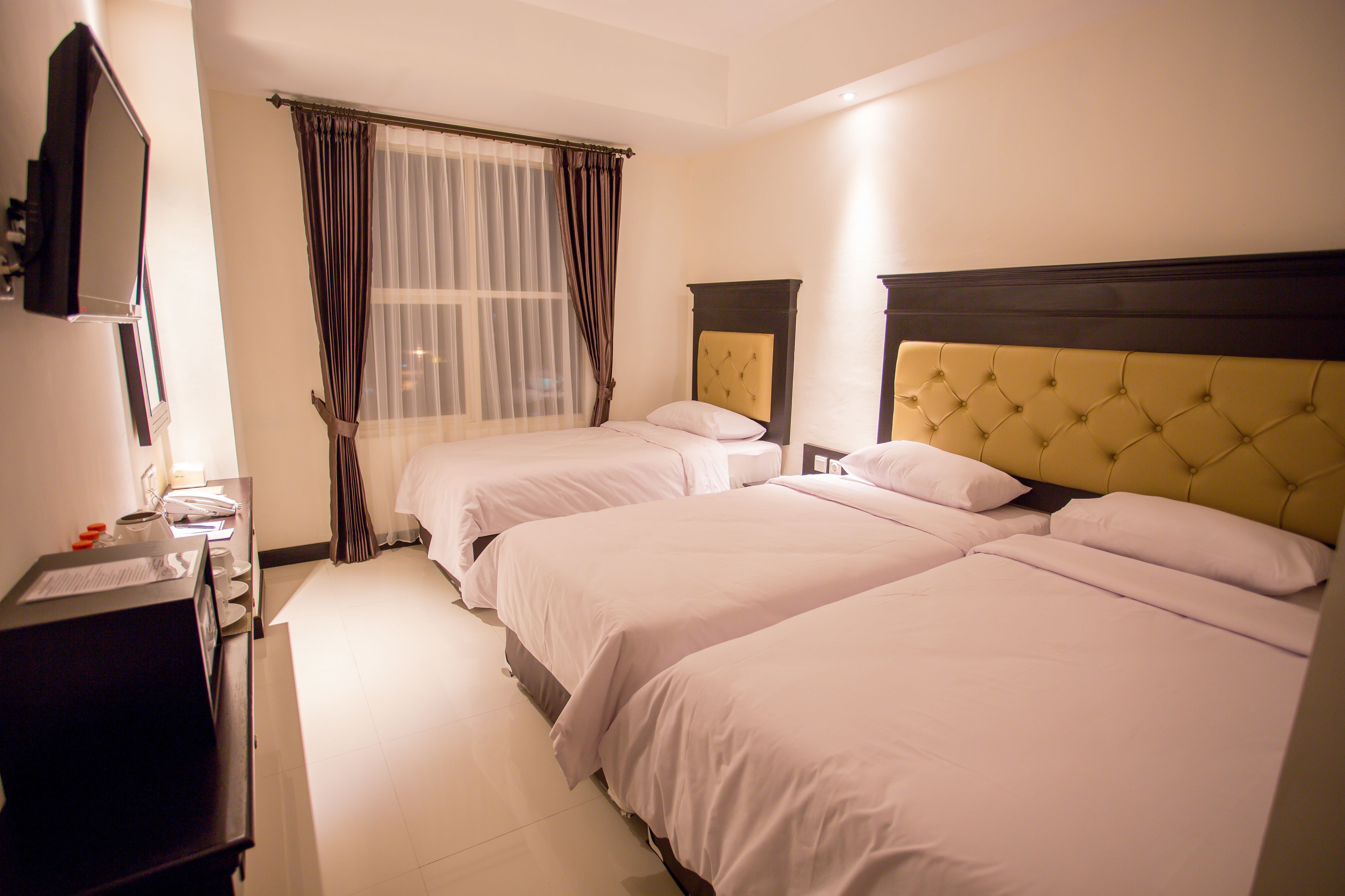A hotel room with two beds, a television, a desk, and a window with curtains.