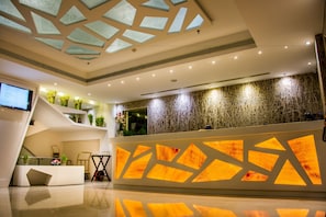 A modern hotel lobby with a reception desk, a staircase, and a ceiling with geometric patterns. - Rockdale Clarks Inn Suites (Visakhapatnam)