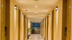 Un couloir d’hôtel avec des portes des deux côtés, un sol carrelé et un plafond doté d’un éclairage encastré.