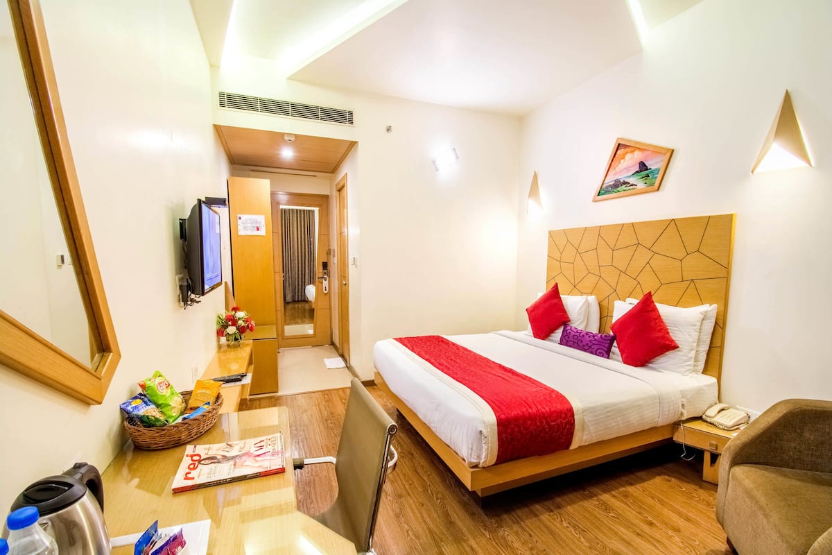 A hotel room with a bed, bedside table, chair, desk, and a television.