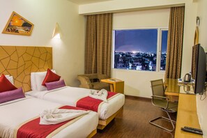 Ett hotellrum med två sängar, ett skrivbord med en stol, en tv och utsikt över staden.