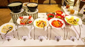 Une table de buffet proposant divers plats, chacun étant clairement identifié, notamment une salade de poulet, un «aloo papdi chat» et une salade de carottes à la noix de coco.