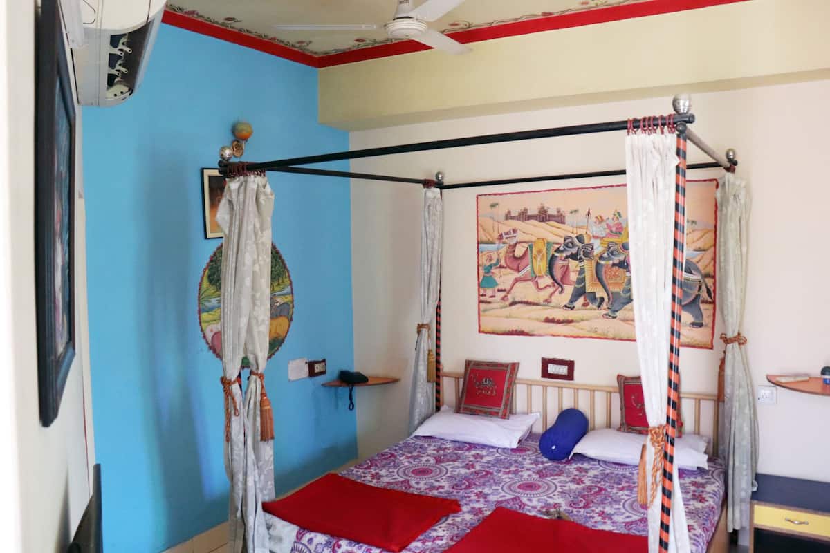 A room with a four-poster bed, a ceiling fan, a wall-mounted air conditioner, and a colorful mural.
