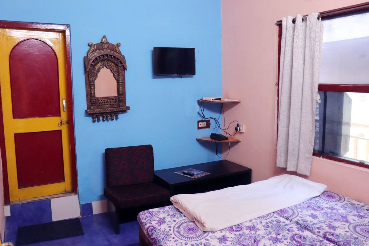 A room with a bed, a chair, a TV, and a door.