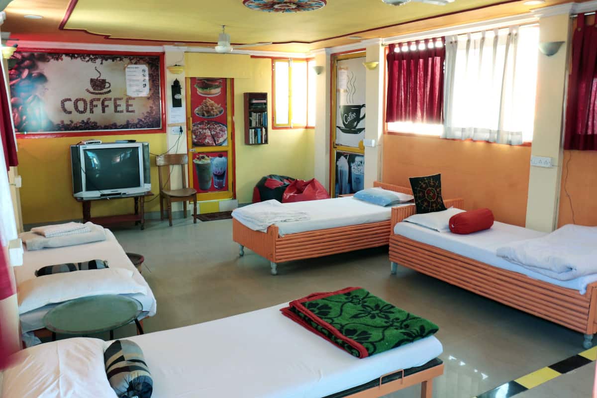 A hotel room with two single beds, a television, a small table, and a sofa.