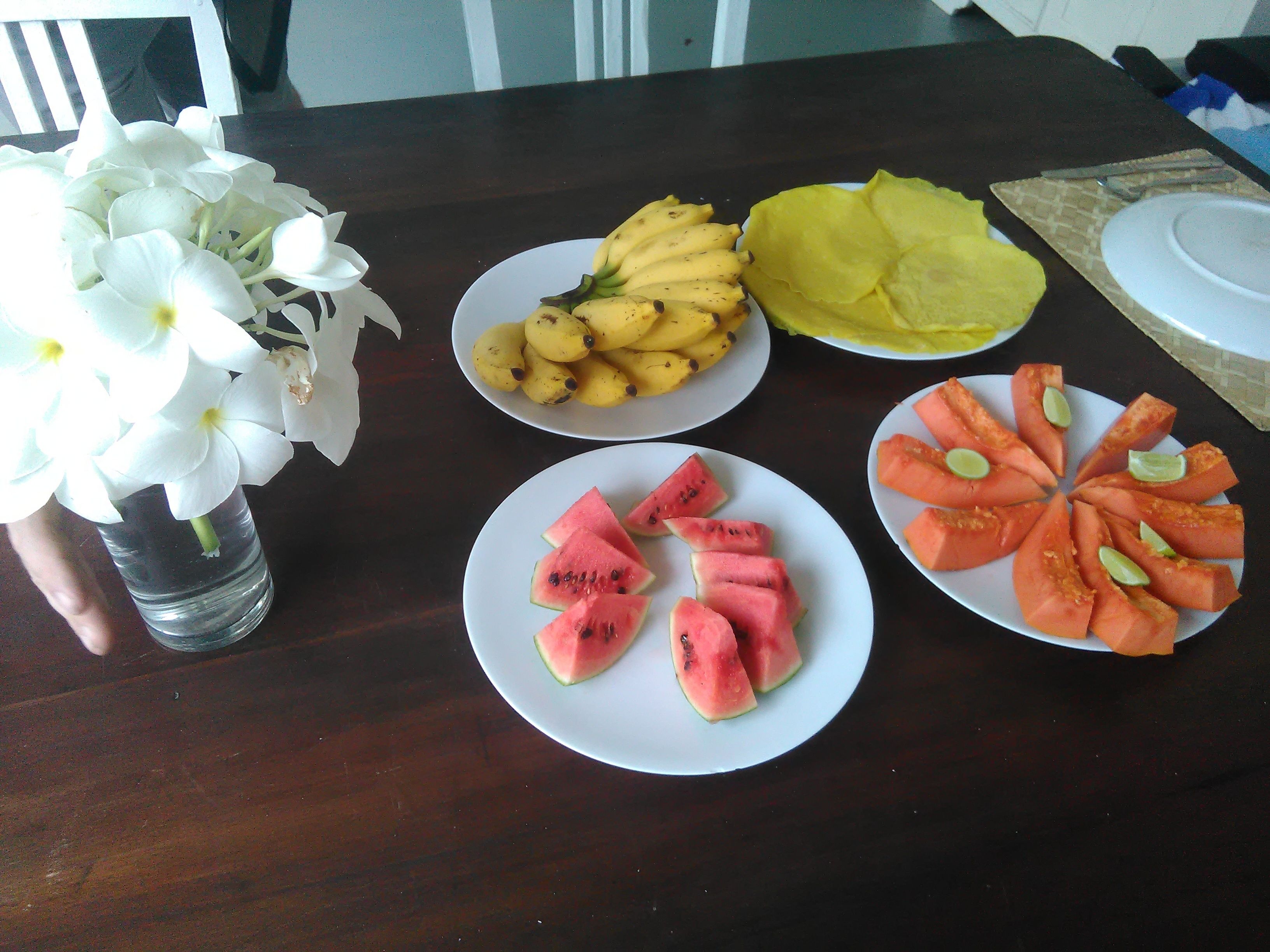 Una mesa de comedor con platos de fruta y un florero de flores.
