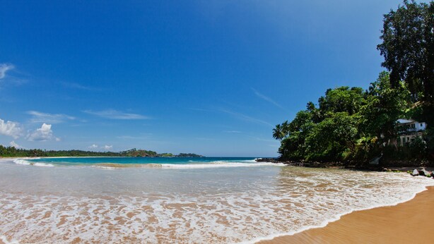 A beach with clear blue water, a sandy shore, and lush greenery. - Talalla Bay Beach House (Talalla)