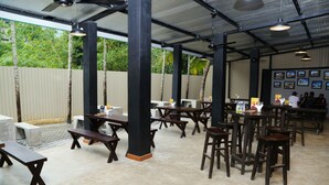 An outdoor restaurant with wooden tables and benches, a covered roof, and a view of greenery. - Paradise Inn (Kandy)