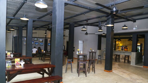 A spacious indoor area with high ceilings, exposed beams, and multiple wooden tables and stools. - Paradise Inn (Kandy)