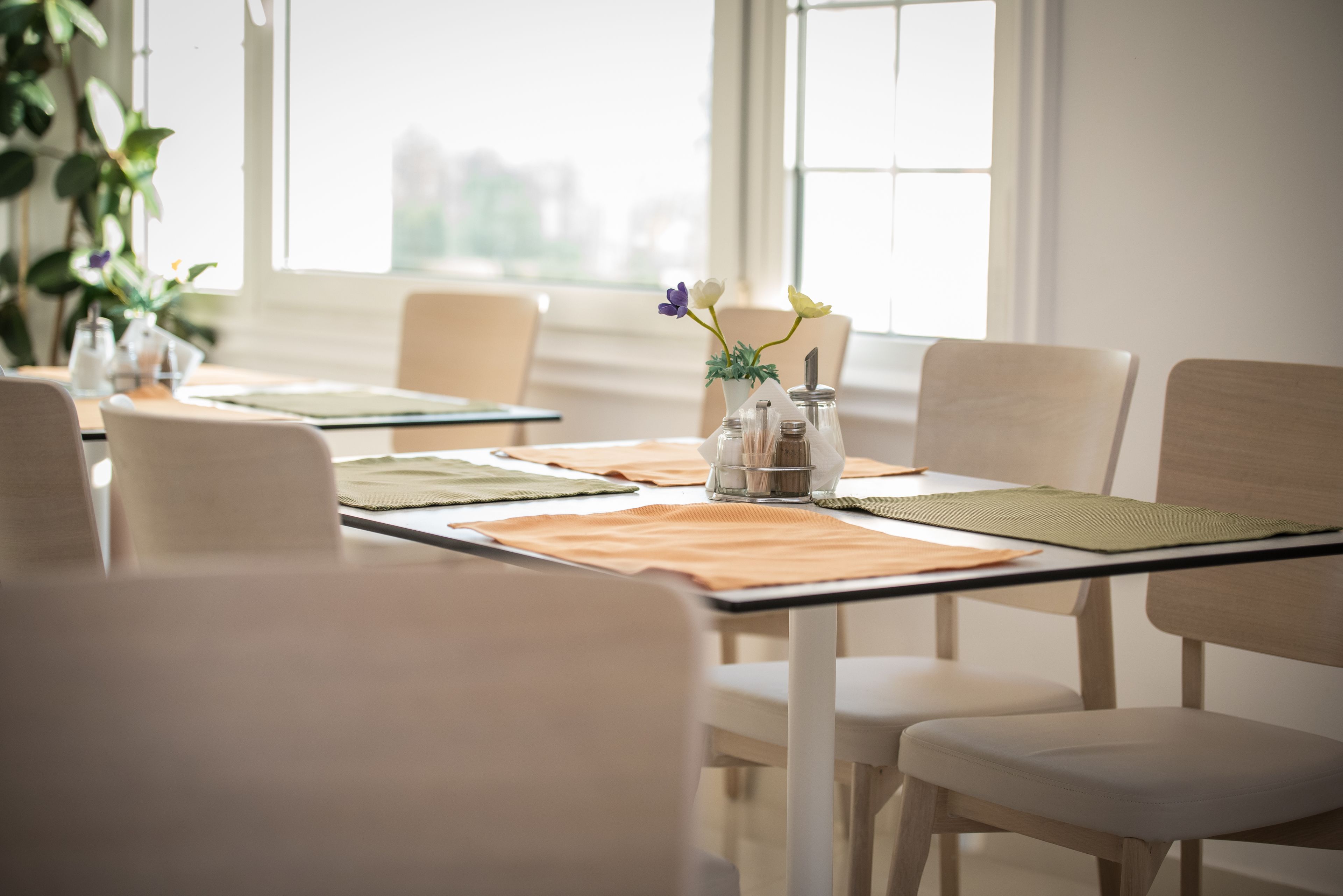 Een eethoek met een tafel voor vier personen, inclusief een vaas met bloemen, een kaars en een menukaart.