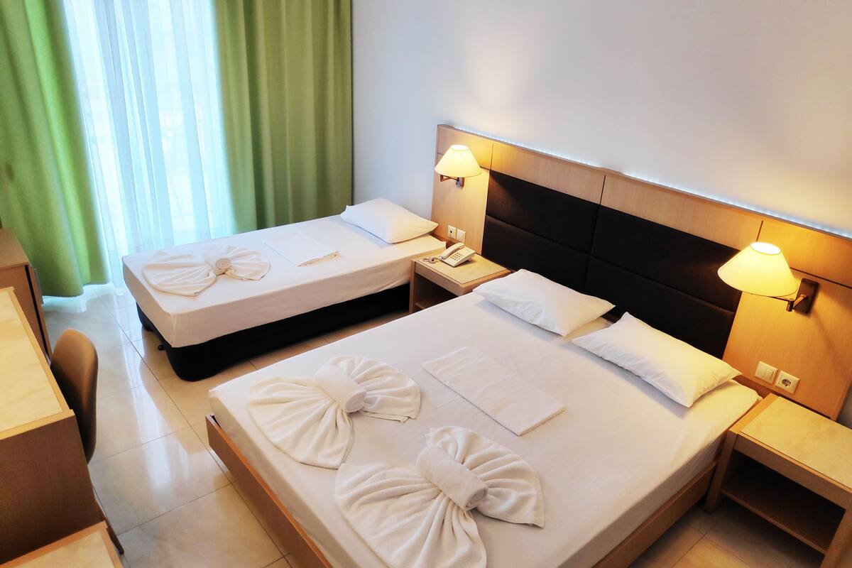 A hotel room with two beds, each with towels and pillows, bedside lamps, and a desk with a chair.