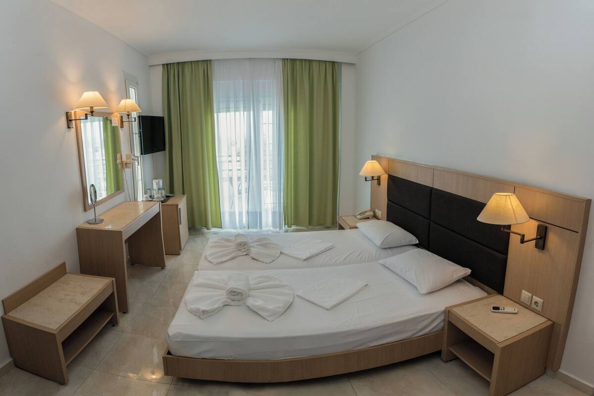 A hotel room with a bed, bedside tables, a desk, a mirror, and a TV.