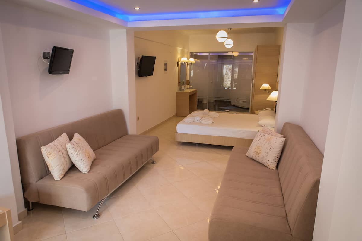 A modern hotel room with a sofa, a bed, a TV, and a bathroom with a mirror and lights.
