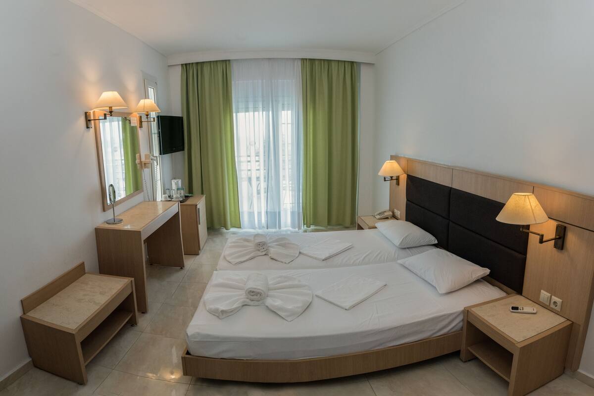 A hotel room with a bed, bedside tables, a desk, a mirror, and a TV.