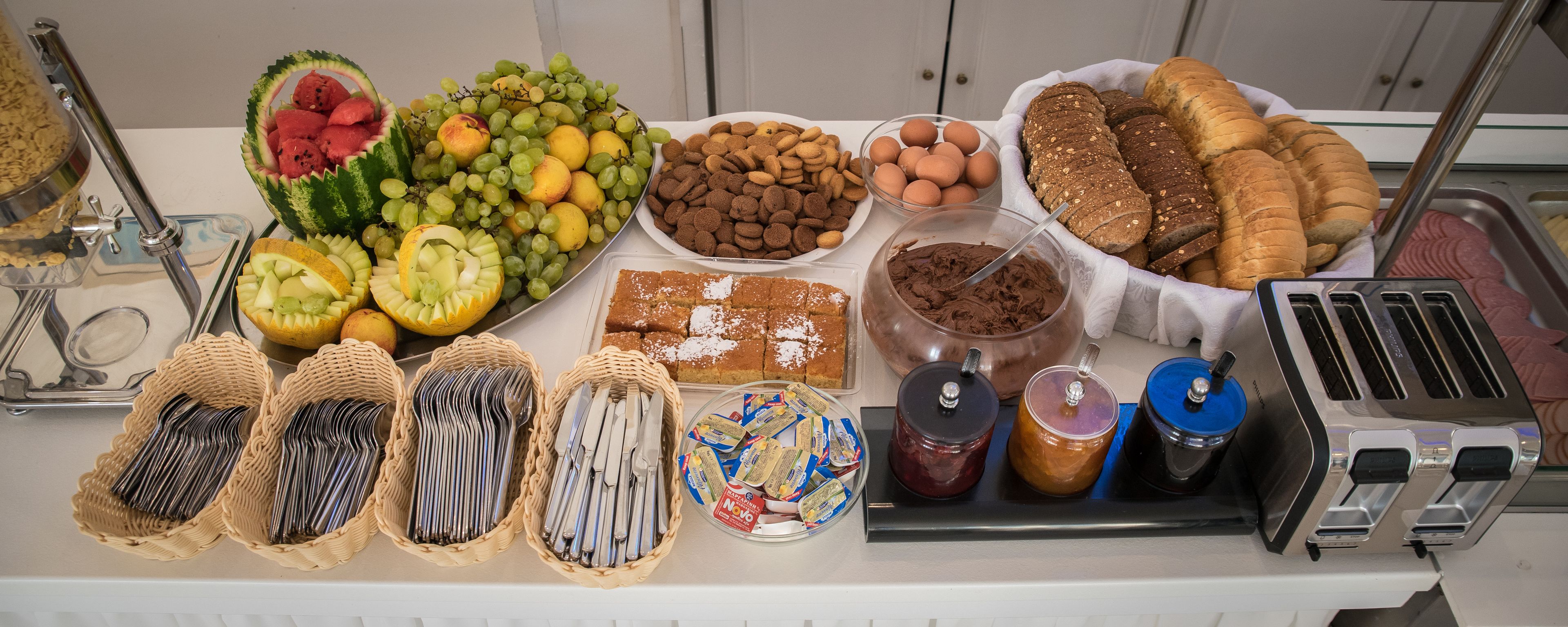 A buffet table with various food items including fruits, bread, and condiments.