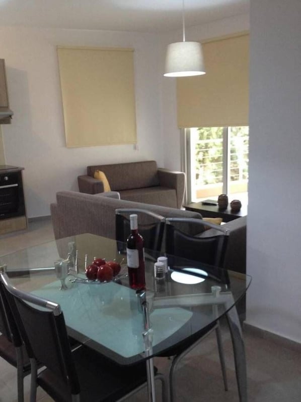 A modern living room with a glass dining table, a sofa, and a large window.