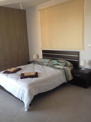 A bedroom with a bed, a nightstand, a wardrobe, and a window with blinds.