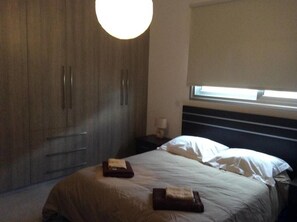Un dormitorio con cama, mesita de noche, lámpara, armario y ventana con persianas.