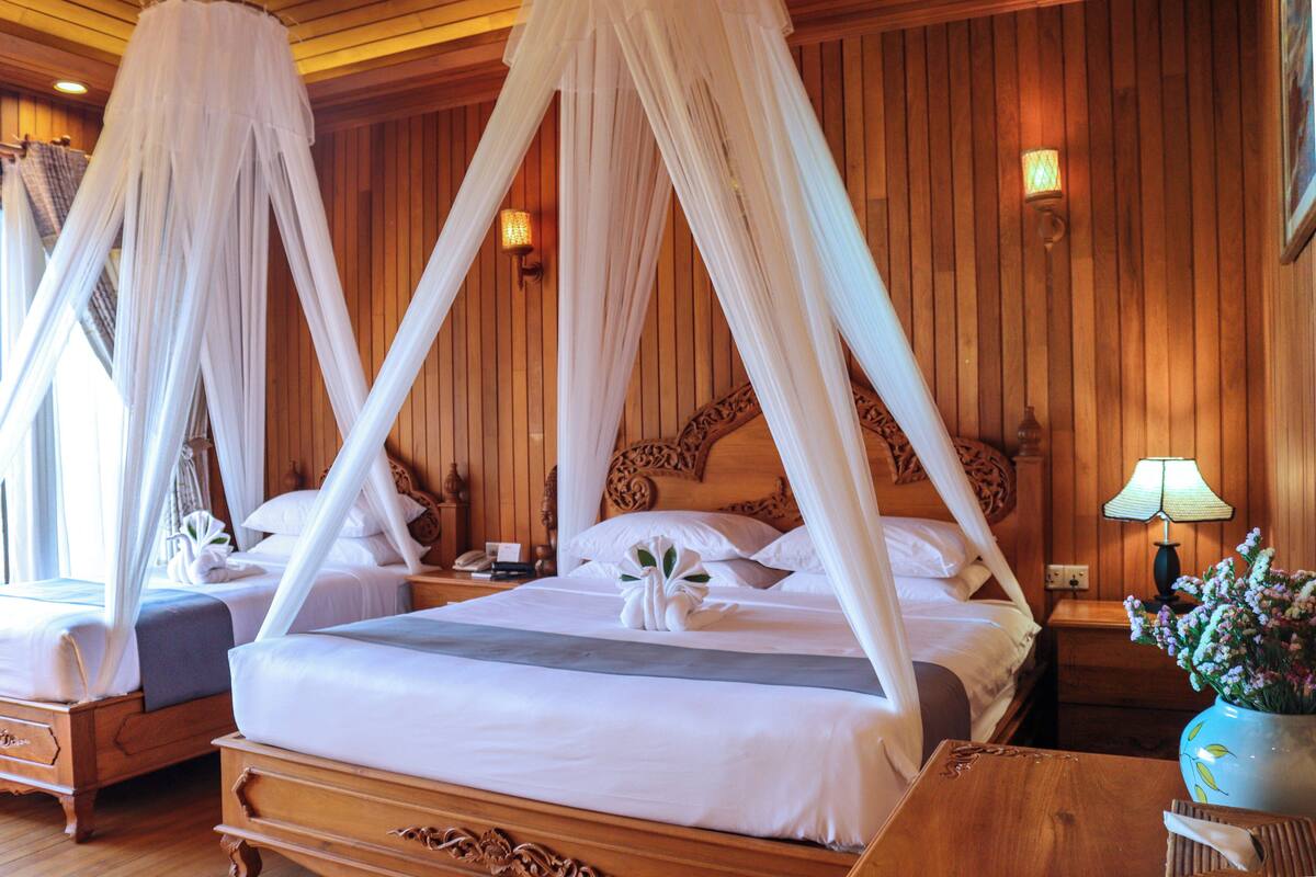 A four-poster canopy bed with white linens, a wooden headboard, bedside tables, and a nightstand with a lamp.