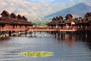 A row of wooden cabins with a lake in the foreground and mountains in the background. - KMA Inle Hotel (Nyaungshwe)