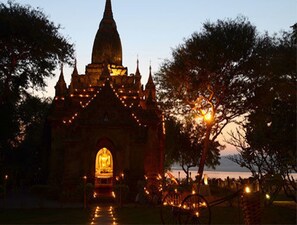 A temple with a central golden statue, surrounded by trees and a body of water.