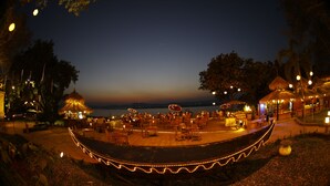 A waterfront restaurant with outdoor seating, a stage, and string lights. - KMA Bagan Hotel River View (Nyaung-U)