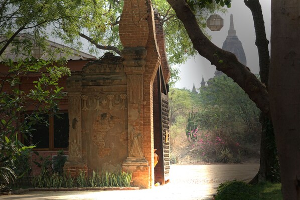 A traditional brick structure with intricate carvings, a large tree, and a distant view of a pagoda.