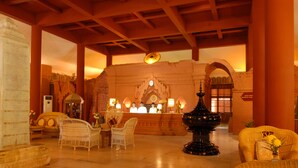 A lobby with a reception desk, wicker chairs, a large black urn, and a brick wall with a clock. - KMA Bagan Hotel River View (Nyaung-U)