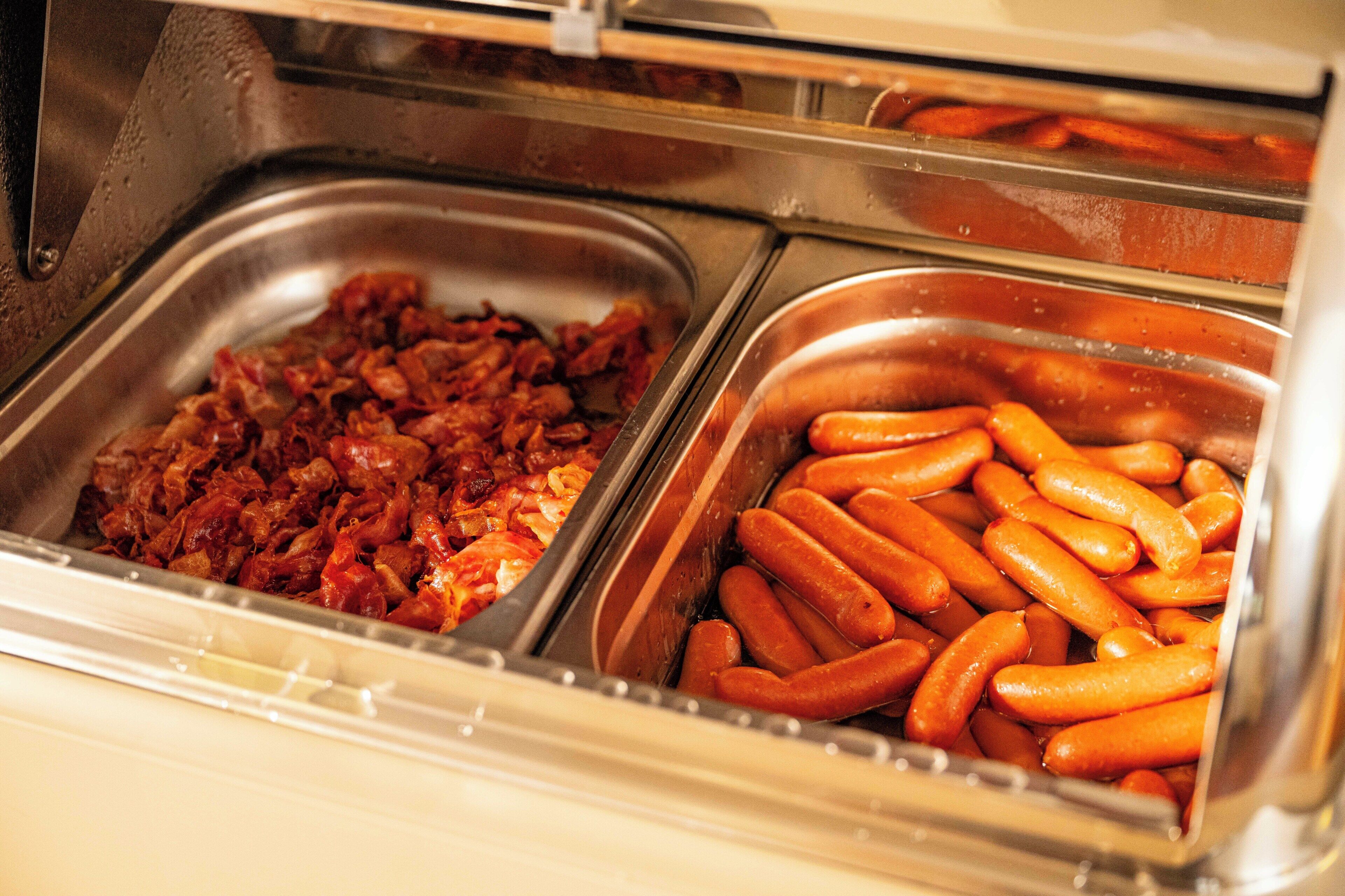 A buffet with two trays of food, one with what appears to be bacon and the other with sausages.