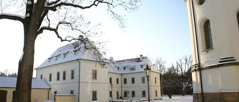 Un edificio cubierto de nieve, con un gran árbol en primer plano y un cielo despejado.