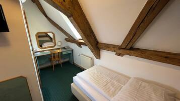 A bedroom with a bed, a desk, a chair, and a mirror.