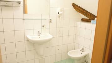 Un baño con lavamanos, bidé y secador de pelo en la pared.