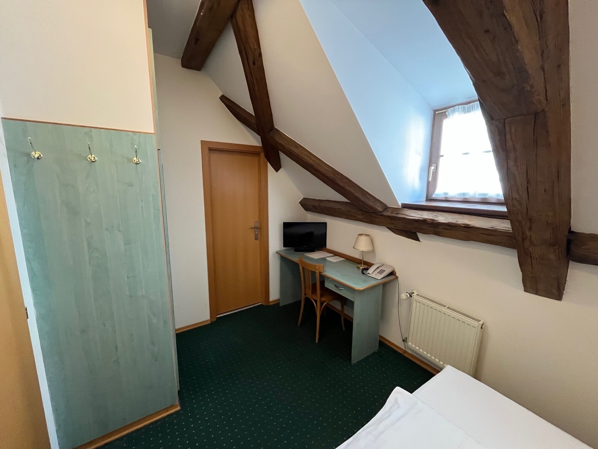 Una habitación con techo inclinado, un escritorio con silla, un televisor y una ventana.