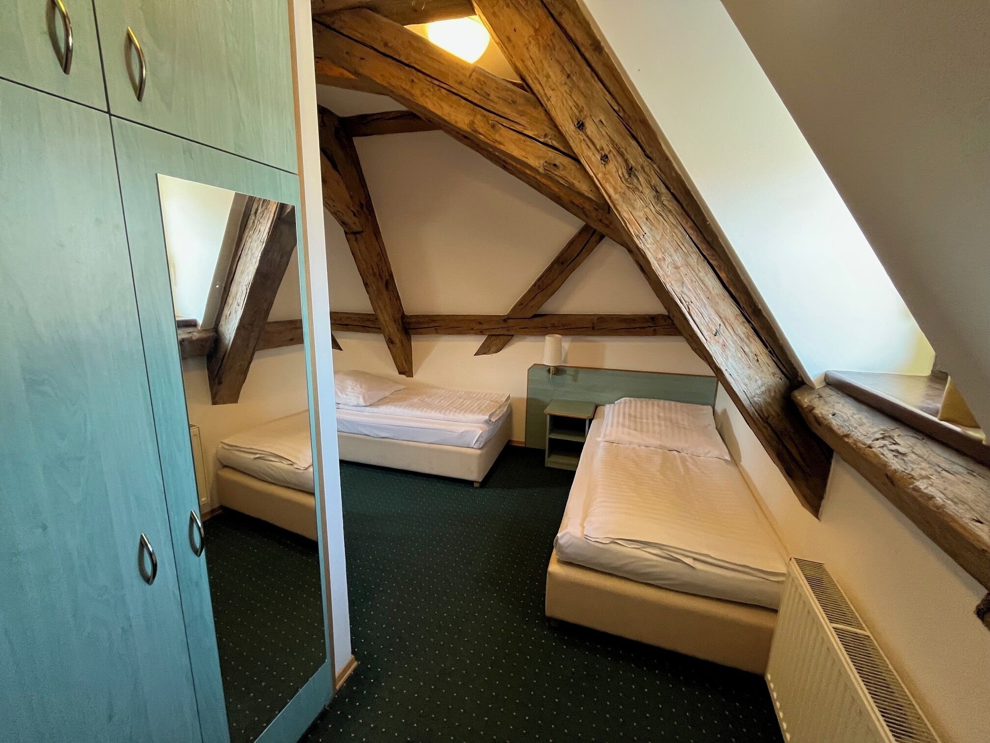A small attic bedroom with two single beds, a wardrobe, and a sloped ceiling with exposed wooden beams.