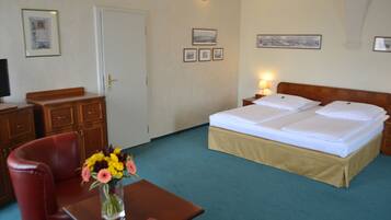 Habitación de hotel con cama, mesitas de noche, un escritorio con silla, un jarrón de flores y una puerta.