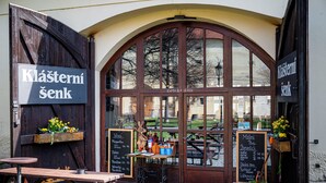 An outdoor seating area with wooden tables and benches, a chalkboard menu, and flower baskets. - Hotel Adalbert (Prague)