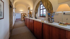 A reception area with a counter, a clock, framed pictures, and a window with curtains. - Hotel Adalbert (Prague)
