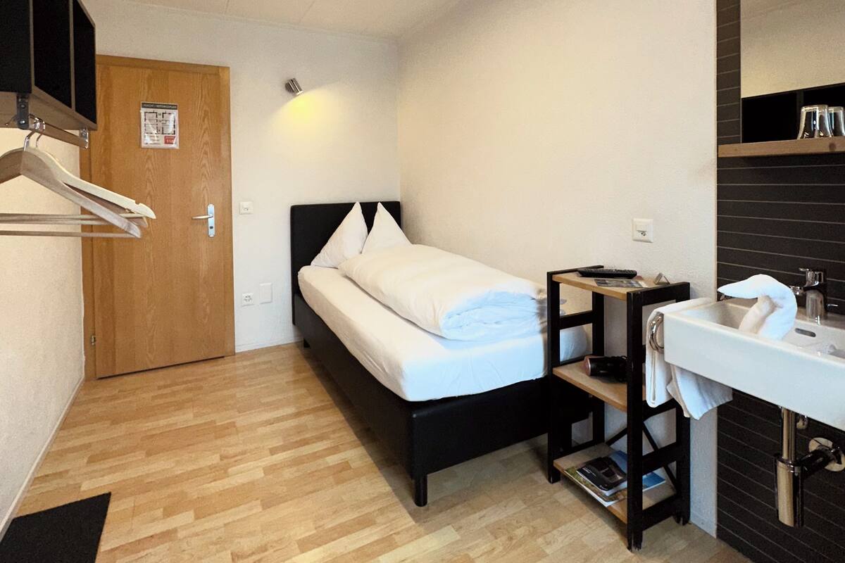 A compact hotel room with a bed, a bedside table, a mirror, and a sink.