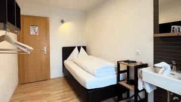 A compact hotel room with a bed, a bedside table, a mirror, and a sink.